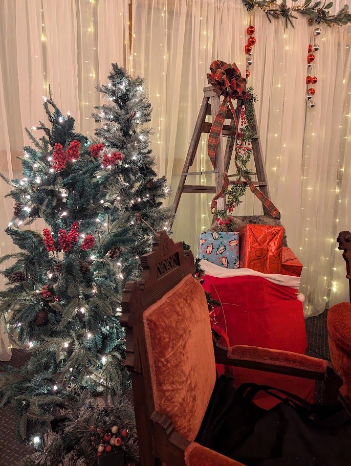 Santa's red velvet chair framed by lit trees and sheer curtains