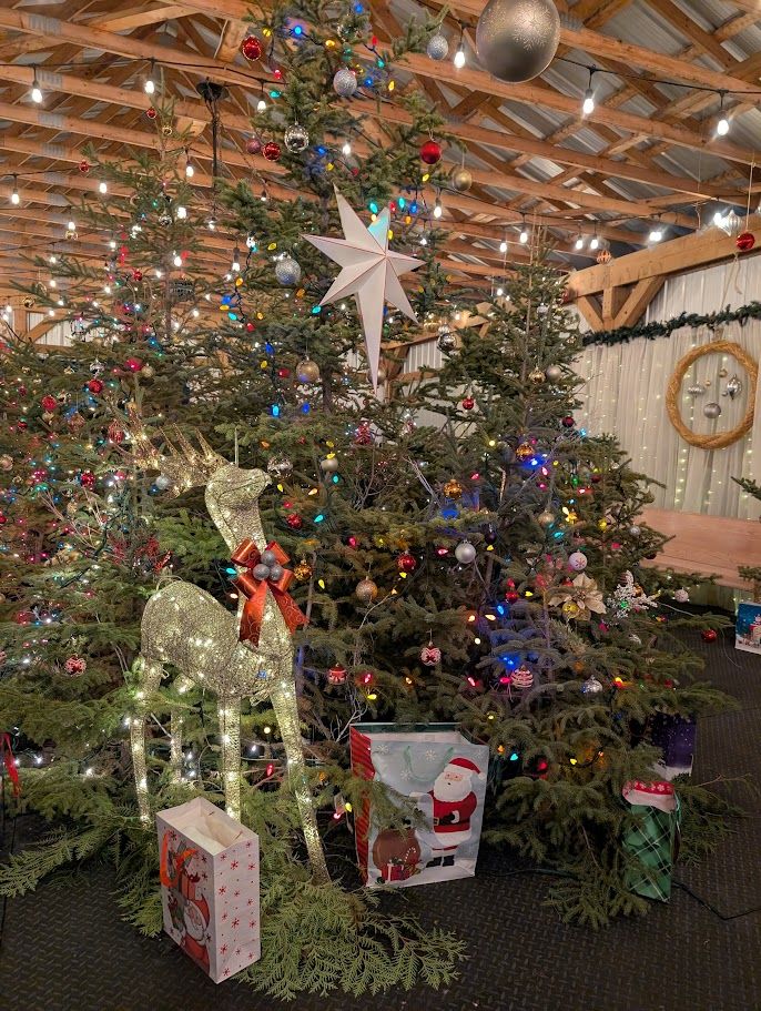 A tall decorated tree with a lit reindeer in Christmas Tree Alley under the covered tent